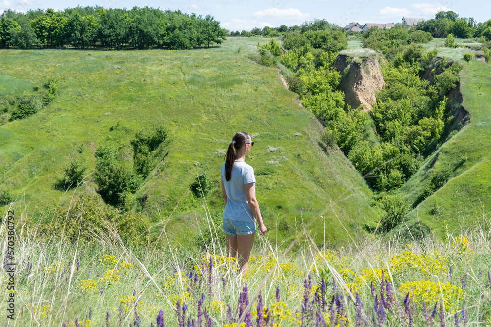 Woman looking on ravine covered with greenery. Young female traveler see landscape valley with geological faults. She admires earthen mountains and relief. Girl explore world. Positive emotion. Woman looking on ravine covered with greenery. Young female traveler see landscape valley with geological faults. She admires earthen mountains and relief. Girl explore world. Positive emotion.