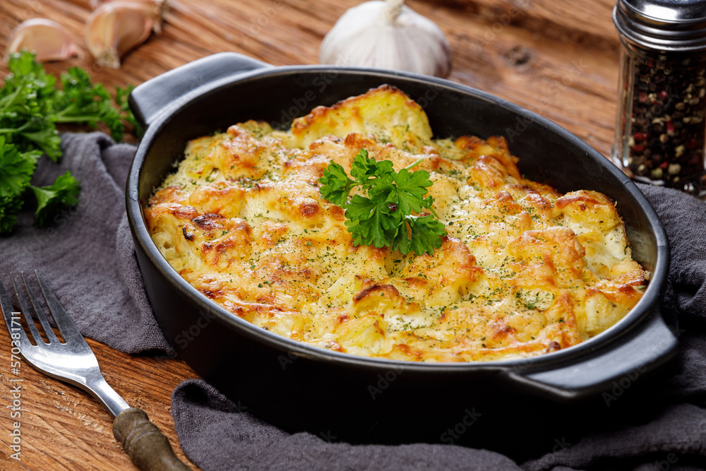 Potato casserole with cheese and parsley on wooden table. French cuisine, close up Potato casserole with cheese and parsley on wooden table. French cuisine, close up