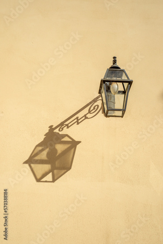 old street lantern on a wall in Elba island, Italy. Projecting an interesting shadow like a painting on the wall. Cast Iron lamp.