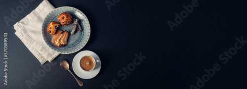 Taza de café con galletas y muffins en plato con cuchara de cobre, sobre fondo banner largo azul oscuro