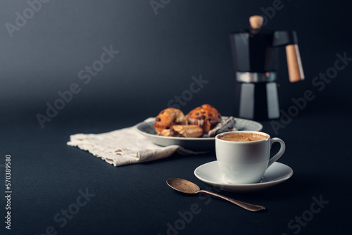 Taza de café con cuchara de cobre, con plato con galletas y muffins de chocolate, cafetera italiana, sobre fondo azul oscuro