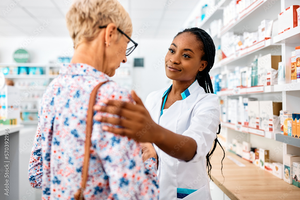 Caring African American pharmacist consoling sad senior woman in drugstore.