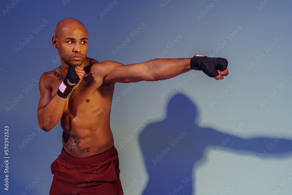 Professional kickboxer is training and practicing punch on studio background with shadows
