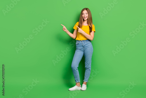 Full length photo of astonished positive girl indicate fingers empty space isolated on green color background