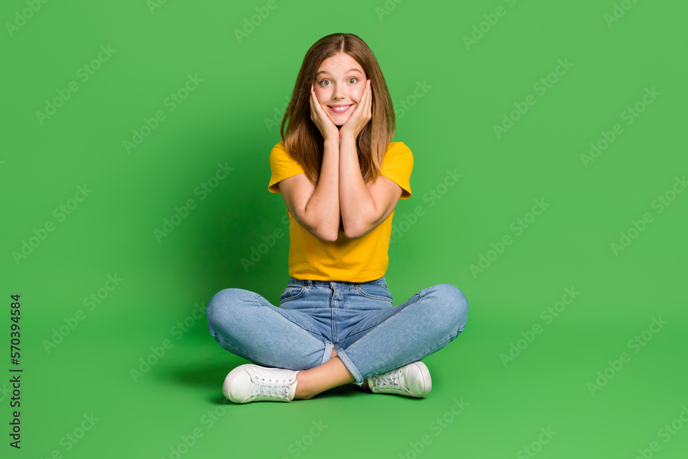 Full length photo of cheerful nice person sit floor arms touch cheeks isolated on green color background Full length photo of cheerful nice person sit floor arms touch cheeks isolated on green color background