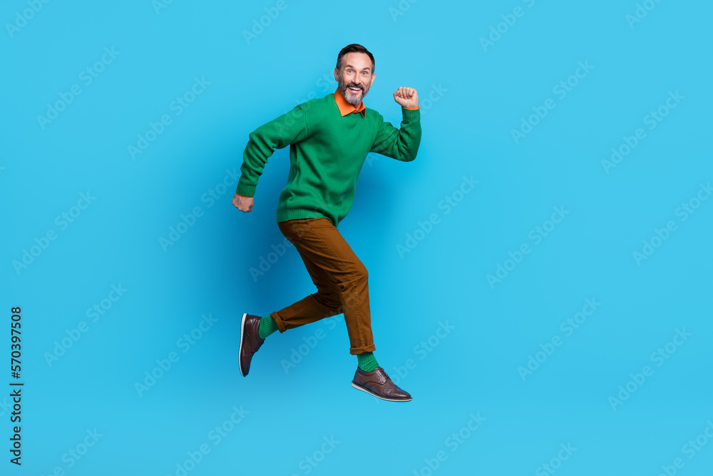 Obraz premium Full length photo of mature nice mister energetic running jumping rush dressed stylish green outfit isolated on blue color background