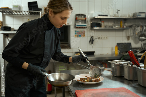 Fototapeta Naklejka Na Ścianę i Meble -  Young woman cook in professional kitchen puts meat on plate