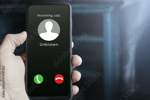 Male hand holding mobile phone showing incoming call from an unknown caller on the screen, with buttons to answer or reject. Possible scammer or spam call. Mobile security and privacy concept. photo