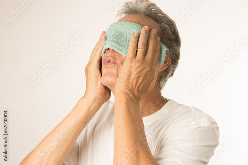 Older man with a warn compress over his eyes for pain relief