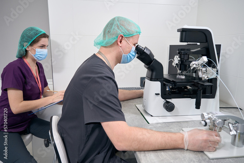 Male embryologist at microscope carries out the fertilization of egg photo