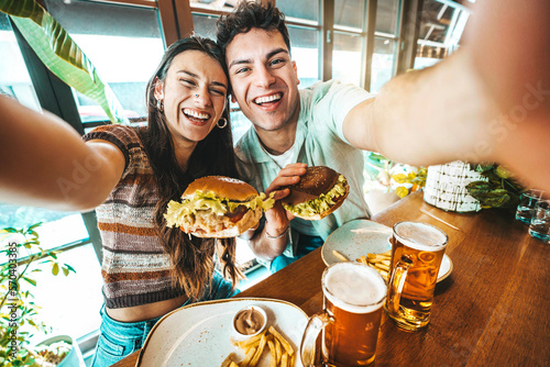 Leinwand Poster Happy couple taking selfie with smart mobile phone at burger pub restaurant - Yo