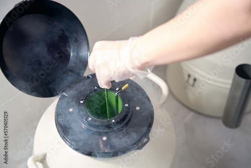 Medical worker in cryo-storage puts biomaterial into tank with liquid nitrogen photo