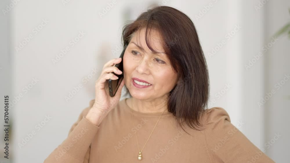 Closeup attractive stylish woman in brown top thin earrings smiling enjoying talking on smartphone sitting in chair Closeup attractive stylish woman in brown top thin earrings smiling enjoying talking on smartphone sitting in chair