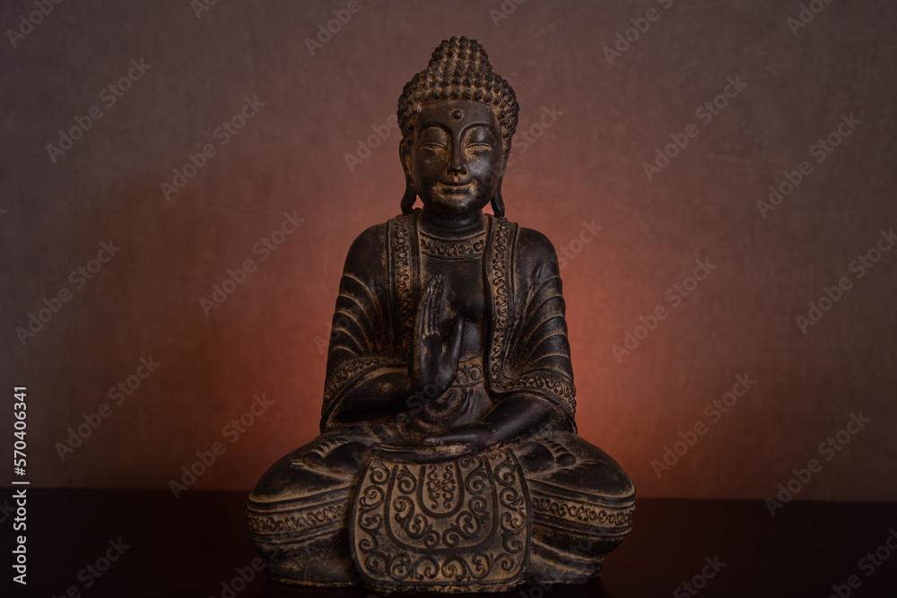 The statue of Buddha sitting in meditation in a dark environment on a golden glowing background illuminated by candlelight