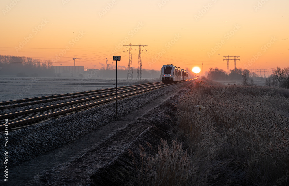 A regional commuter train in the countryside during a winter sunrise.