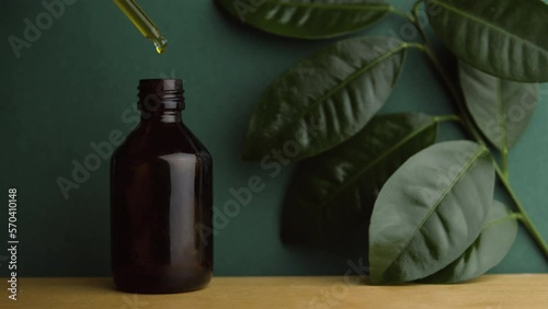 Natural oil. Alternative medicine. Handmade cosmetics. A pipette with oil. Dark glass bottle on a wooden table. Background from natural leaves. A drop of oil.  Face and body skin care. 