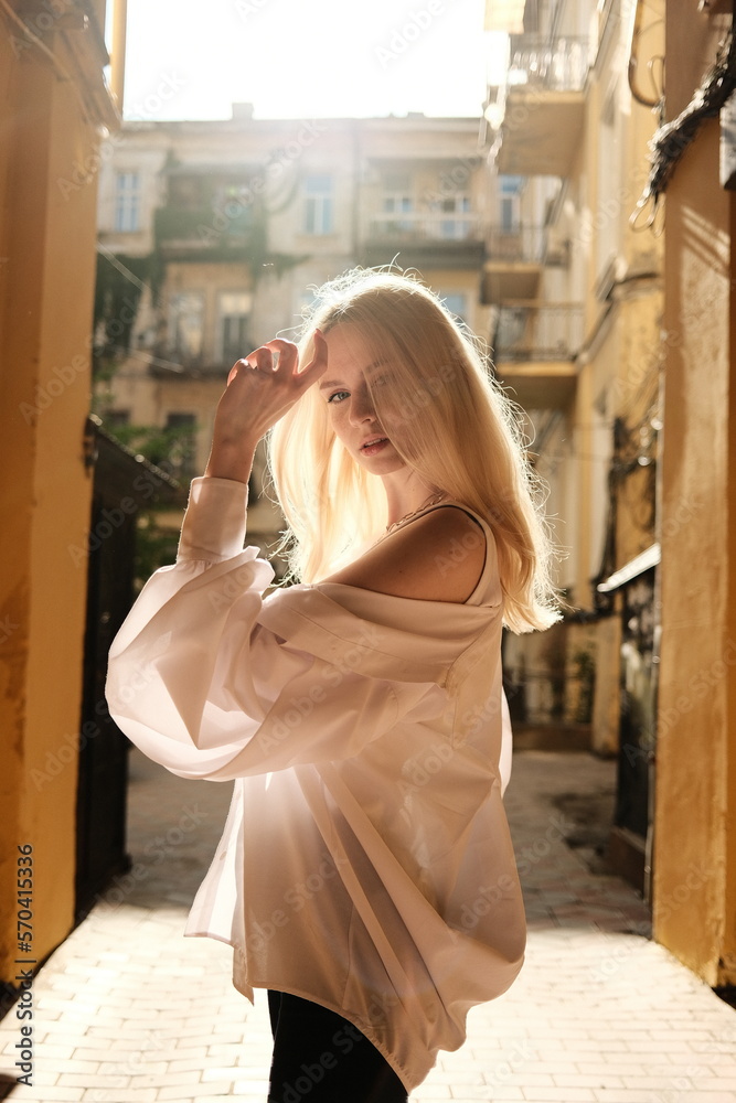 Fototapeta premium The blonde girl feels light and relaxed in city in the sun. The beauty of youth. 