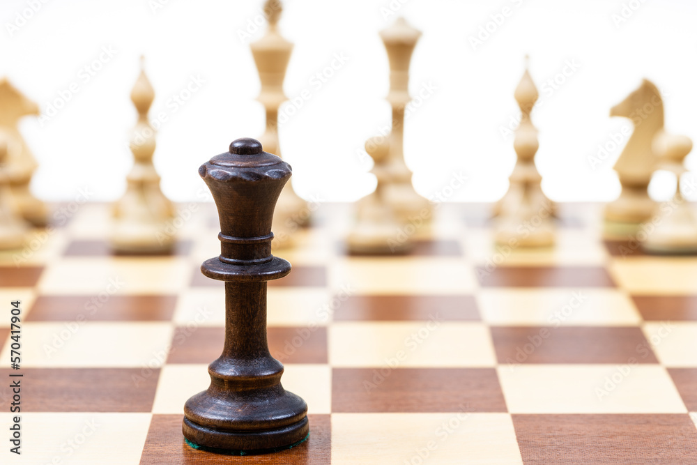 black queen against white chess figures in background on wooden chessboard close up (focus on queen) black queen against white chess figures in background on wooden chessboard close up (focus on queen)