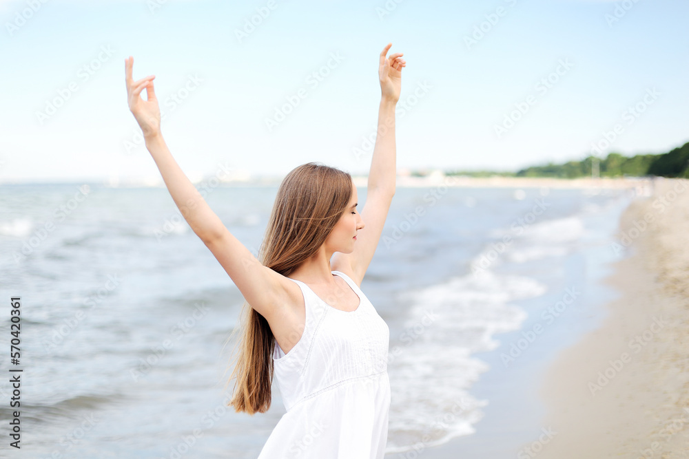 Happy smiling woman in free happiness bliss on ocean beach standing with raising hands. Portrait of a multicultural female model in white summer dress enjoying nature Happy smiling woman in free happiness bliss on ocean beach standing with raising hands. Portrait of a multicultural female model in white summer dress enjoying nature
