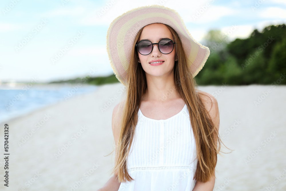 Portrait of a happy smiling woman in free happiness bliss on ocean beach standing with a hat and sunglasses. A female model in a white summer dress enjoying nature 
