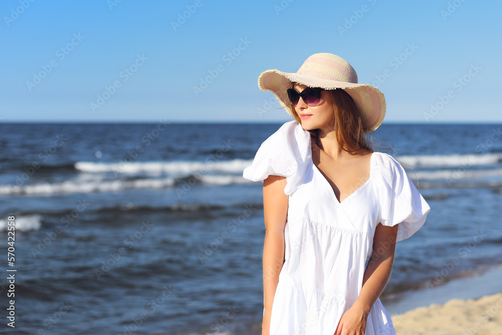 Happy smiling blonde woman is posing on the ocean beach with sunglasses and a hat Happy smiling blonde woman is posing on the ocean beach with sunglasses and a hat