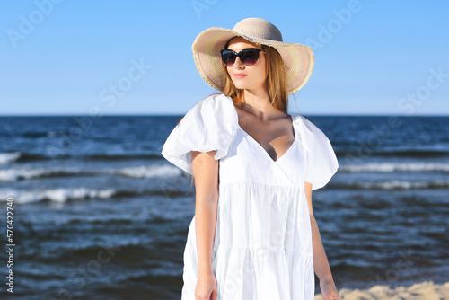 Happy blonde woman is posing on the ocean beach with sunglasses and a hat. Evening sun © rogerphoto