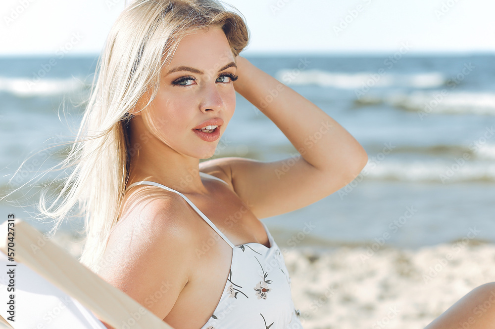 Happy blonde woman relaxing on a wooden deck chair at the ocean beach