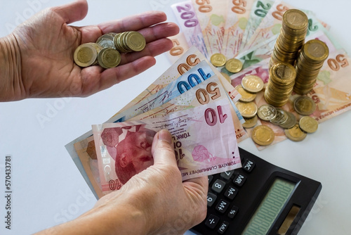 Hand holding Turkish Lira Banknote and coins, on pile of coins and calculator photo