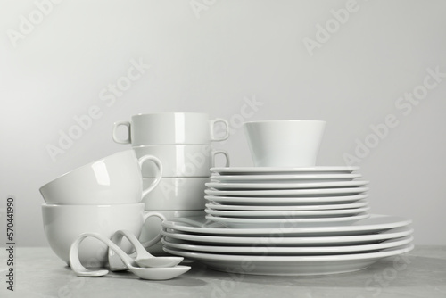 Set of clean dishware on grey table against light background