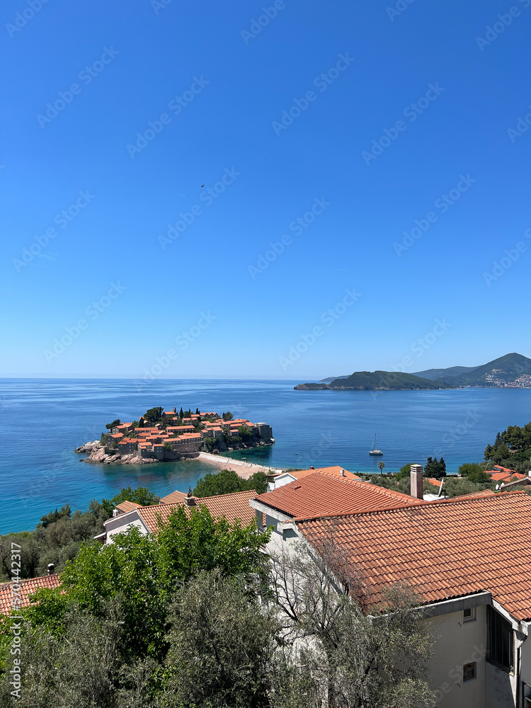 View of the island of Sveti Stefan in the Bay of Kotor over the roofs of old coastal houses. Montenegro