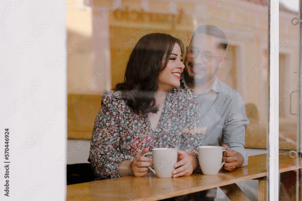 Young couple drinking coffee in a coffee shop - Hispanic man and woman laughing and having fun while having coffee Young couple drinking coffee in a coffee shop - Hispanic man and woman laughing and having fun while having coffee