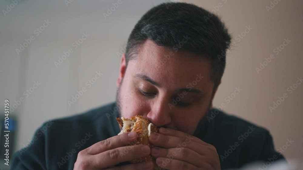 Young hungy man eats a hamburger with his mouth wide open Young hungy man eats a hamburger with his mouth wide open