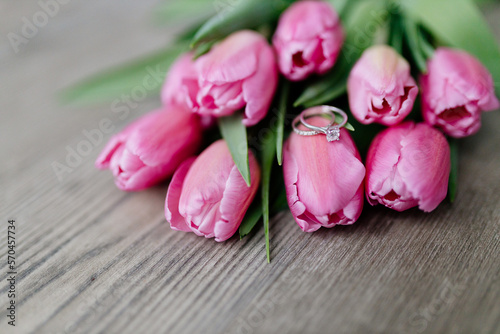 Pink tulips and engagement rings with diamonds lie on a wooden background. Background for Valentine's Day. Gift for Mother's Day or Women's Day