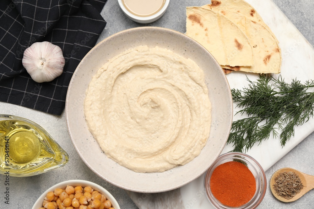Bowl with delicious hummus and different ingredients on light grey table, flat lay
