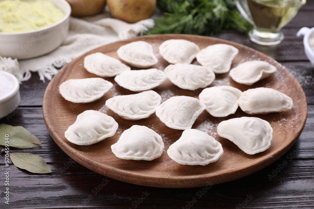 Raw dumplings (varenyky) and ingredients on brown wooden table