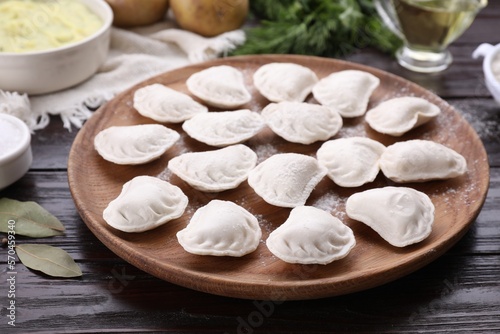 Raw dumplings (varenyky) and ingredients on brown wooden table