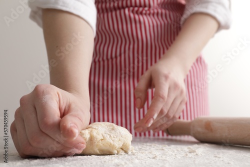 Woman kneading fresh dough at light grey table, closeup