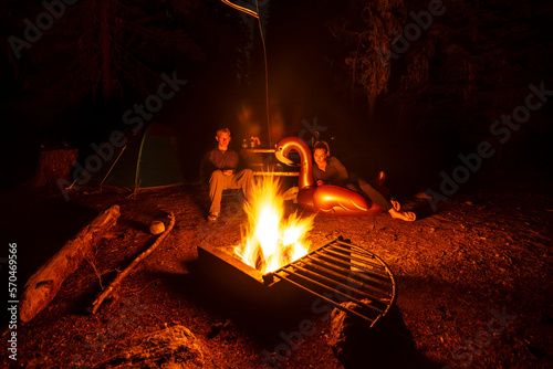 Adventurous athletic man and women sitting around a campfire, at their camp at night. 