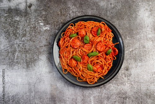 Homemade Sausage and tomato pasta with basil leaves on a round plate on a dark background. Top view, flat lay