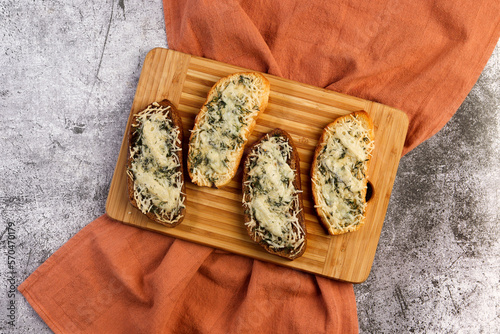 Garlic and melted cheese grilled sandwiches with herbs on a cutting wooden board on a dark grey background. Top view, flat lay