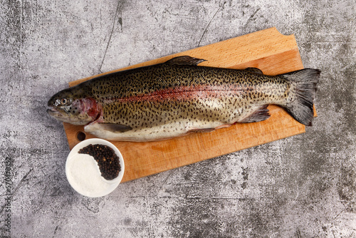 Raw rainbow trout on a cutting wooden board on a dark grey background. Top view, flat lay