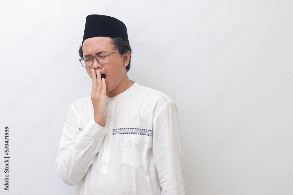 Portrait of young Asian muslim man yawning with hand covering his mouth. Isolated image on white background Portrait of young Asian muslim man yawning with hand covering his mouth. Isolated image on white background