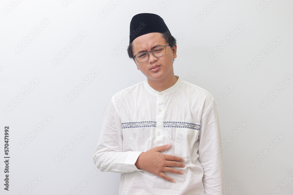 Portrait of young Asian muslim man feeling pain in his stomach. Stomachache concept. Isolated image on white background Portrait of young Asian muslim man feeling pain in his stomach. Stomachache concept. Isolated image on white background
