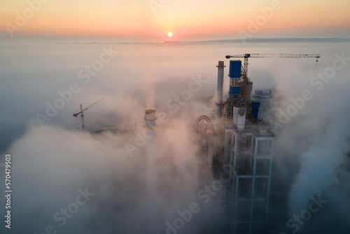 Aerial view of cement factory with high concrete plant structure and tower crane at industrial manufacturing site on foggy evening. Production and global industry concept © bilanol