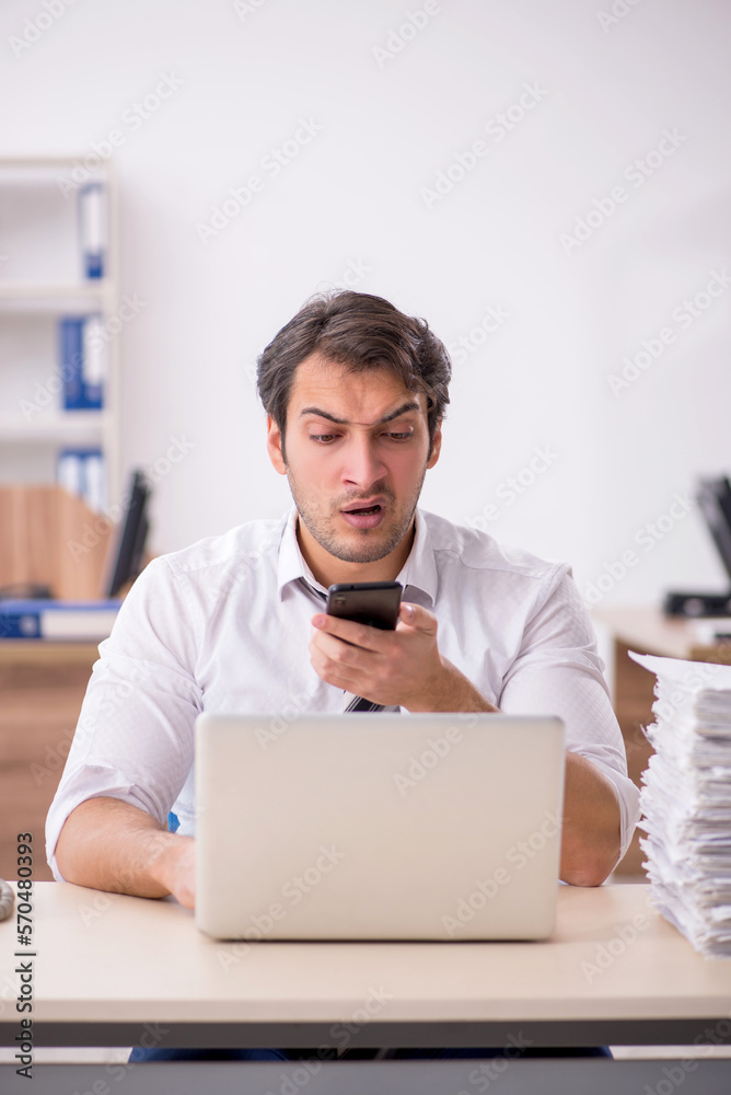 Young male employee unhappy with excessive work in the office Young male employee unhappy with excessive work in the office