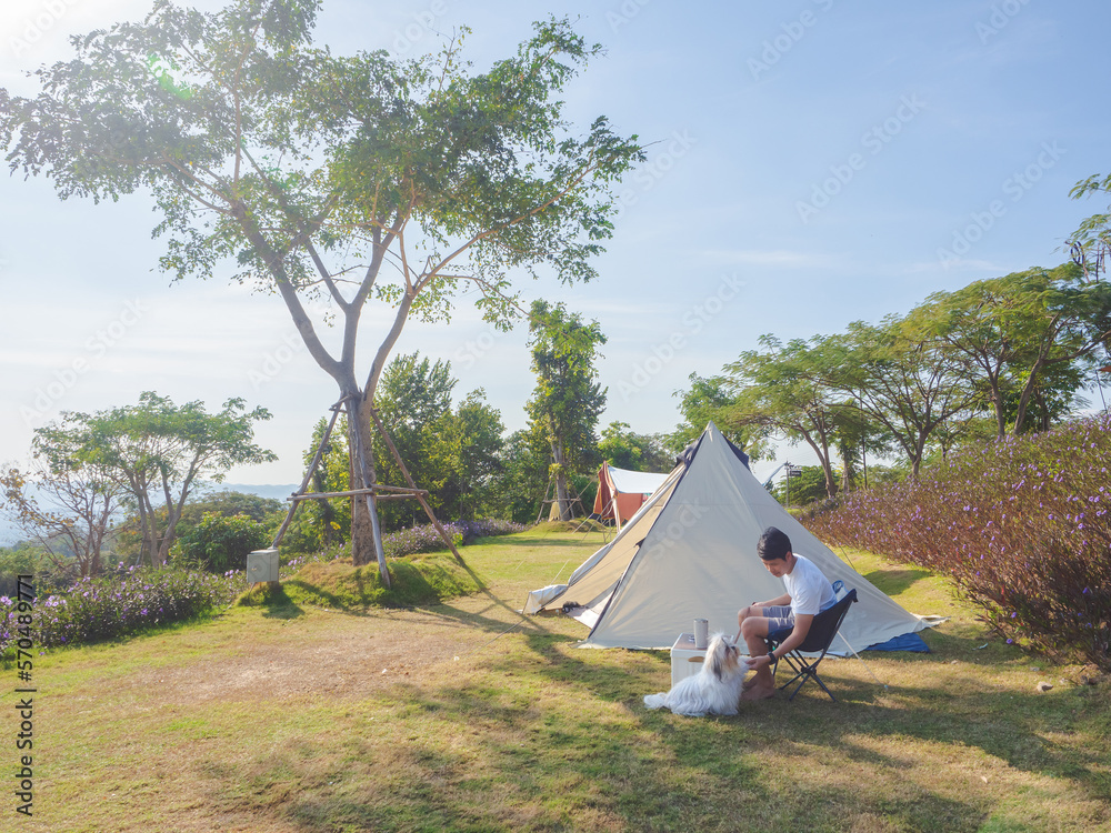 Asian man with cute dog happy and enjoying life camping on grassy hill with mountain view.