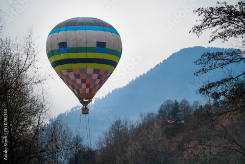 Hot air balloon with fire heating air in wicker basket with himalaya mountains in background showing this adventure in kullu manali valley photo