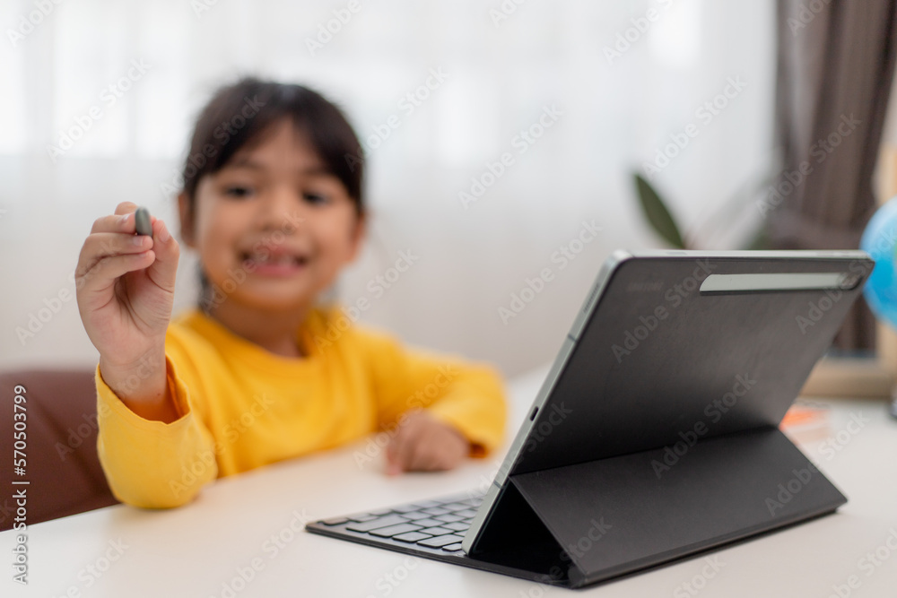 Asian schoolgirl doing her homework with digital tablet at home. Children use gadgets to study. Education and distance learning for kids. Homeschooling during quarantine. Stay at home Asian schoolgirl doing her homework with digital tablet at home. Children use gadgets to study. Education and distance learning for kids. Homeschooling during quarantine. Stay at home