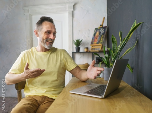 Business video conferencing. Middle-age beard man having video call via computer in the home office. Virtual house party. Happy mature business man executive waving hand using laptop computer photo