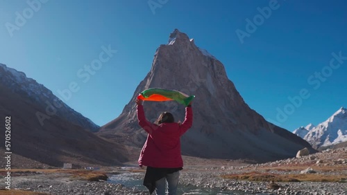 Wide angle shot of female Indian traveler holding Indian flag above her head in front of Gumbok Rangan mountain at Zanskar, Ladakh, India. Indian flag waving in the wind. Indian flag background
 photo